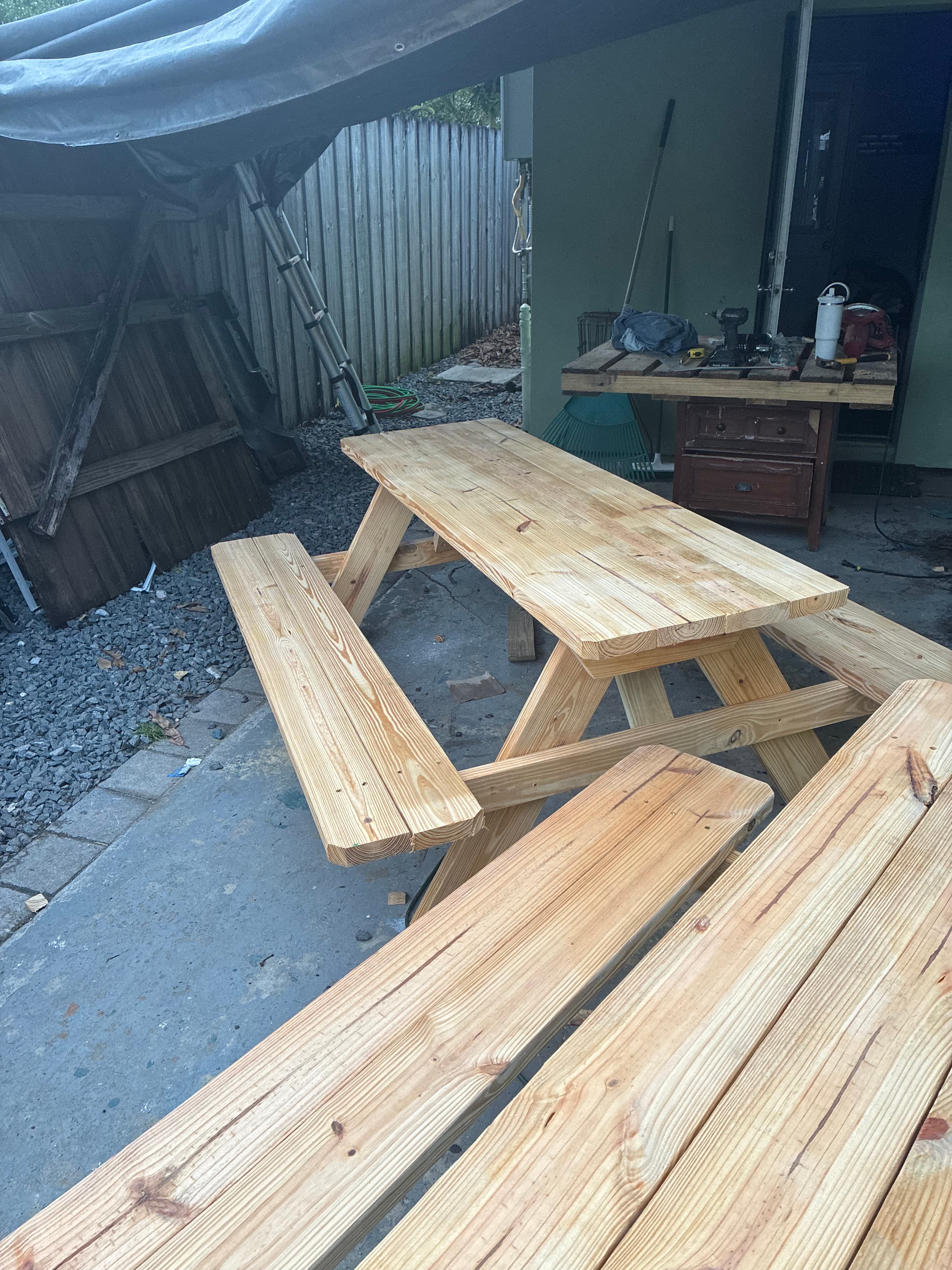 Handcrafted light wood picnic table and benches on a concrete patio under a tarp.